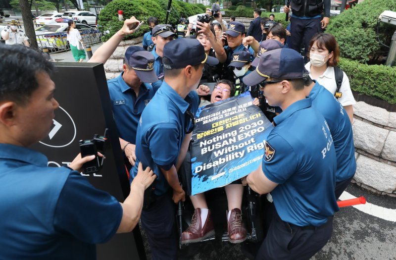 전국장애인차별철폐연대(전장연)이 12일 서울 중구 롯데호텔 지하주차장 출구에서 한덕수 국무총리와의 면담을 요청하며 시위를 벌이자 경찰이 휠체어를 탄 한 전장연 회원을 통행로 밖으로 들어 옮기고 있다. 한 총리는 이날 같은 장소에서 열린 정보보호의 날 기념식에 참석했다. 2023.7.12/뉴스1 ⓒ News1 허경 기자 /사진=뉴스1