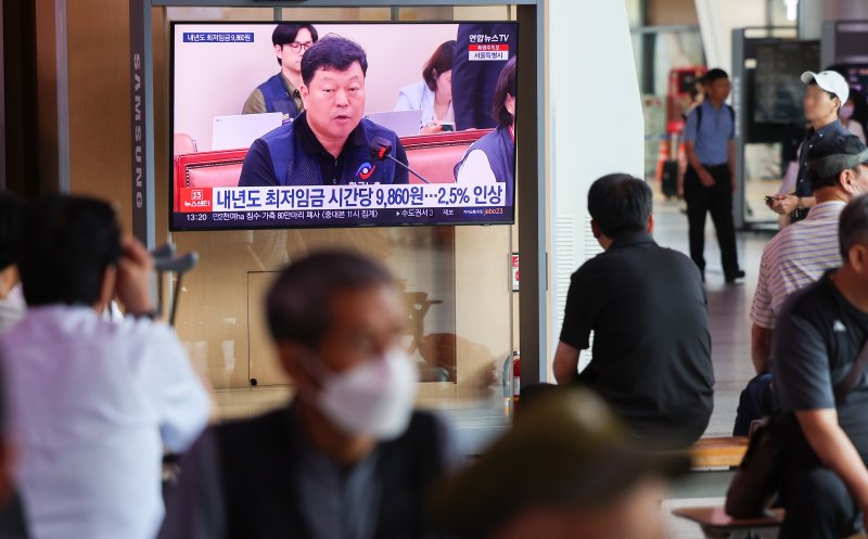 내년도 최저임금이 시급 9860원으로 결정된 19일 시민들이 서울역 대합실에서 TV로 관련 뉴스를 지켜보고 있다. 연합뉴스