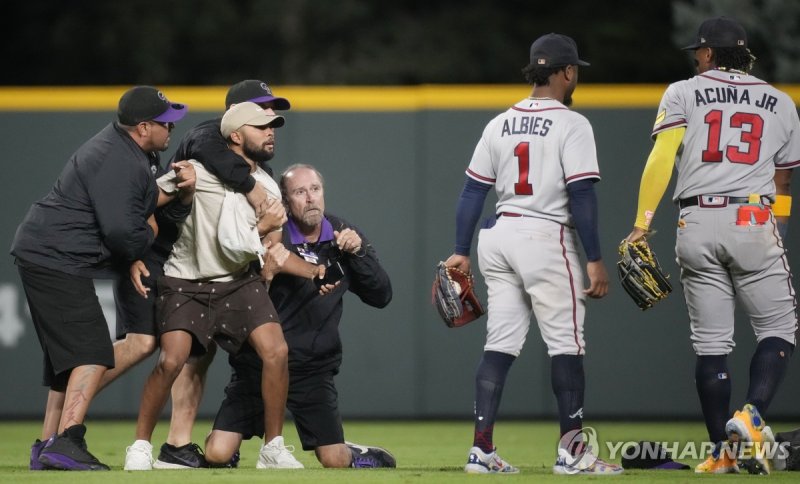 아쿠냐 주니어에게 돌진한 팬을 붙잡은 보안 요원들 Field guards hold onto a fan as he tries to reach Atlanta Braves right fielder Ronald Acuna Jr., right, while second baseman Ozzie Albies (1) looks on in the seventh inning of a baseball game against the Colorado Rockies, Monday, Aug. 28, 2023, in Denver. (AP Photo/David 