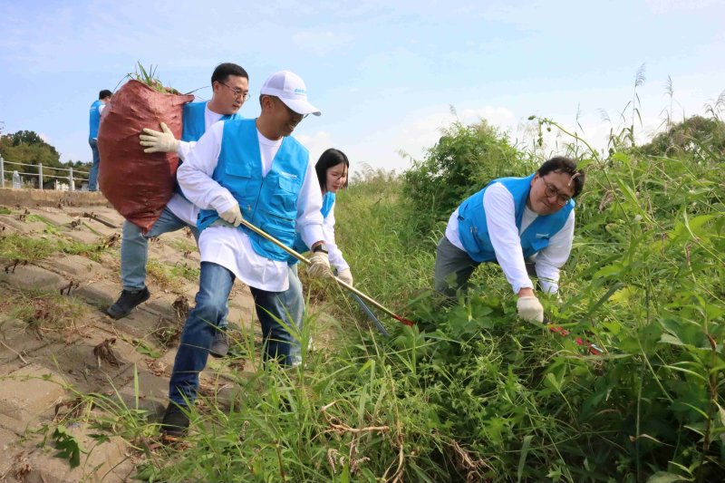 두산밥캣 임직원들이 지난 12일 경기 성남 탄천 주변의 유해식물을 제거하는 지역 봉사활동을 하고 있다. 두산밥캣 제공