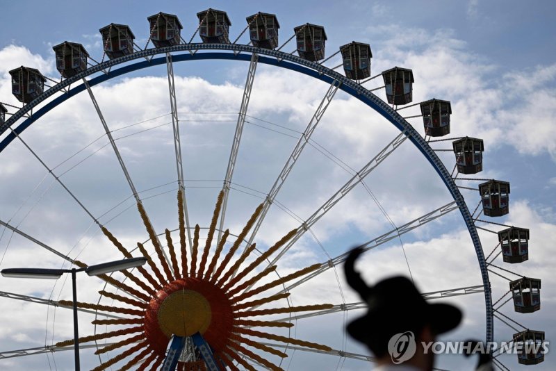 A man with a traditional hat walks in front of a ferris wheel at the Oktoberfest 2023, Munich's annual beer festival, on September 17, 2023 in Munich, southern Germany. The world biggest beer festival Oktoberfest will be open until October 3, 2023 at Munich's Theresienwiese fair grounds. (Photo by T