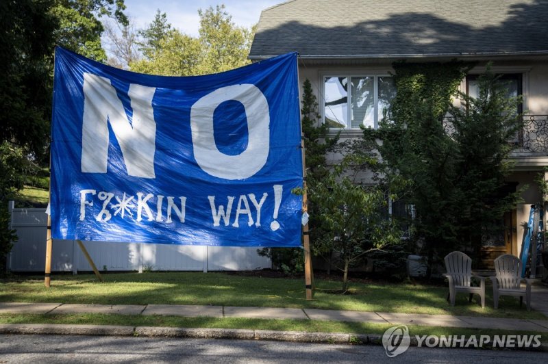 뉴욕의 이민자 임시숙소 예정지 주변 주택에 설치된 반대 현수막 A protest sign stands on the lawn of Scott Herkert beside the former Saint John Villa Academy that has been repurposed as a shelter for homeless migrants, Wednesday, Sept. 13, 2023, in the Staten Island borough of New York. (AP Photo/John Minchillo)