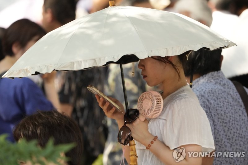 지난해 8월, 일본 도쿄의 긴자에서 한 여성이 양산과 휴대용 선풍기, 선글라스를 들고 있다. 연합뉴스