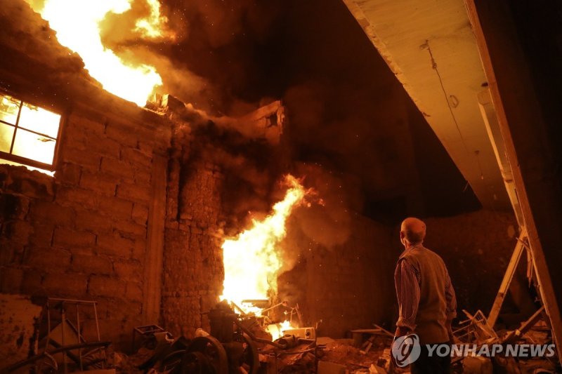 2018년 시리아에서 백린탄을 동원한 폭격에 불타는 주택 epa06622183 A man looks at a burning building after alleged air strikes using white phosphorus in Douma, Syria, 23 March 2018. According to local reports, several buildings have been burning after more than 25 air strikes were carried out on Douma overnight and early 