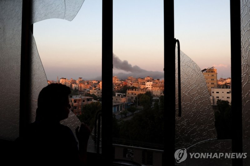 깨진 창문 너머로 이스라엘 공습 지켜보는 팔` 어린이 A Palestinian child watches as smoke billows on the horizon after an Israeli air strike in Gaza City on October 13, 2023. Israel has called for the immediate relocation of 1.1 million people in Gaza amid its massive bombardment in retaliation for Hamas's attacks, with t