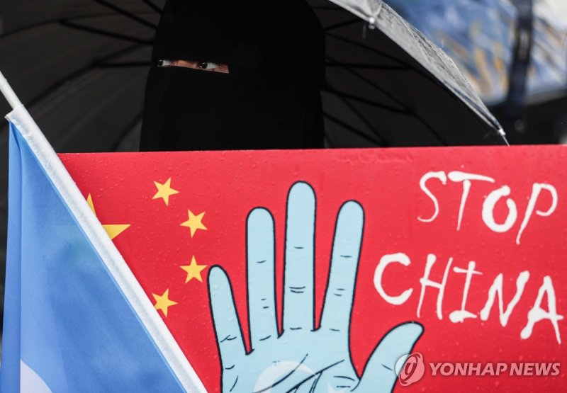 튀르키예 이스탄불의 중국영사관 앞에서 한 여성이 지난해 10월 1일 얼굴을 가린 채 중국의 위구르 족에 대한 탄압 중지와 위구르 인들의 독립을 지지하는 플래카드와 깃발을 들고 시위를 벌이고 있다. EPA연합뉴스
