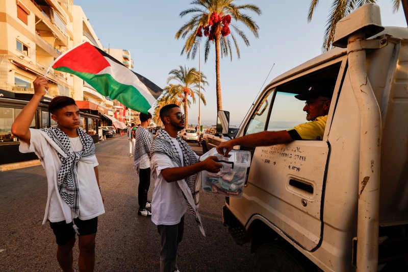 25일(현지시간) 레바논 남부도시 티르에서 팔레스타인 국기를 든 자원봉사자들이 팔레스타인 가자지구의 구호 활동을 위한 모금을 하고 있다.로이터뉴스1