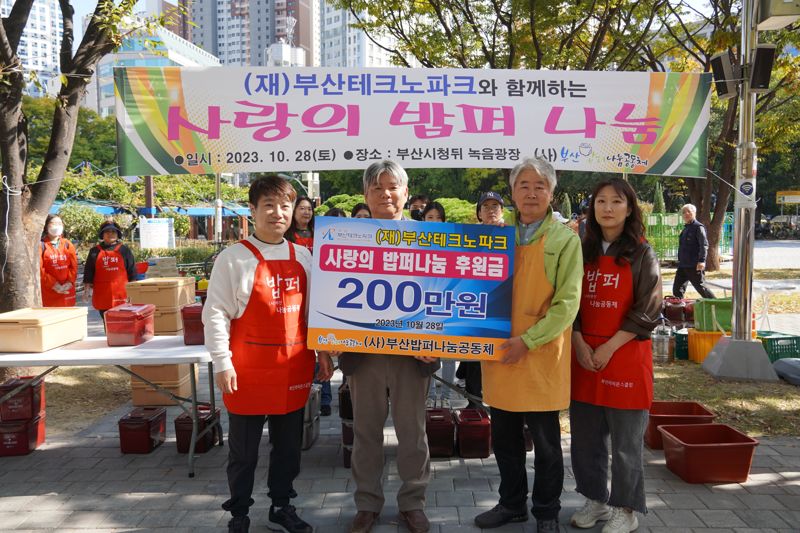 김태훈 부산TP 노조지부장, 김영부 부산TP 정책기획단장, 손규호 부산밥퍼나눔공동체 이사장, 이보원 부산TP 여직원회 회장(왼쪽부터)이 28일 시청 녹음광장에서 사랑의 밥퍼 나눔 무료급식 봉사활동에 참여해 기부금을 전달하며 기념촬영을 하고 있다. 부산테크노파크 제공