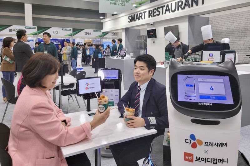 [서울=뉴시스] CJ프레시웨이가 지난해 10월 개최된 '푸드 솔루션 페어 2023'에서 관람객들이 '스마트레스토랑' 코너에서 제공하는 로봇 조리 메뉴를 시식하고 있다. (사진=CJ프레시웨이 제공)