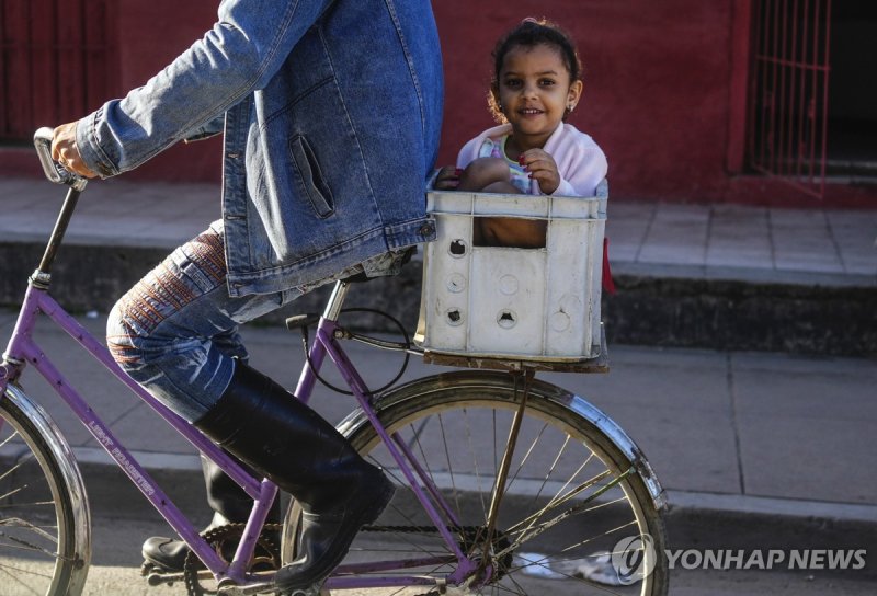 자전거에 올라탄 쿠바 어린이 A girl sits inside a crate as she rides in the back of a bicycle in Sibanicu, Cuba, Saturday, Feb. 10, 2024. (AP Photo/Ramon Espinosa)