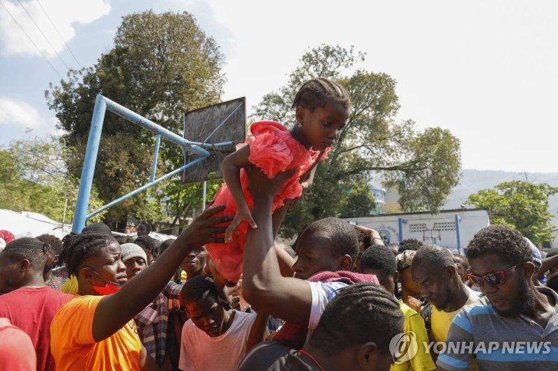 "제 딸에게 먼저 음식을" A father lifts his daughter to the front of a line of people waiting to receive a plate of food, at a shelter for families displaced by gang violence in Port-au-Prince, Haiti, Thursday, March 14, 2024. (AP Photo/Odelyn Joseph)