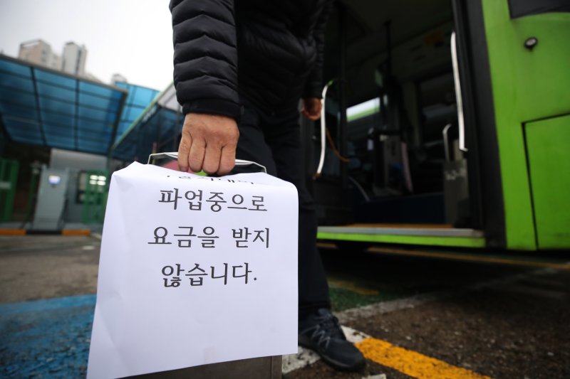 서울 시내버스 노조가 파업에 돌입한 28일 서울의 한 공영차고지에서 일부 운행 버스의 기사가 '파업중으로 요금을 받지 않습니다'라는 게시물이 붙은 요금통을 들고 이동하고 있다. 뉴스1