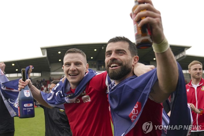기뻐하는 렉섬 선수들 Wrexham's Paul Mullin and Elliot Lee on the pitch celebrating promotion to League One after the final whistle of the Sky Bet League Two match at the SToK Cae Ras, Wrexham, Saturday April 13, 2024. (Jacob King/PA via AP) UNITED KINGDOM OUT; NO SALES; NO ARCHIVE; PHOTOGRAPH MAY NOT BE STOR