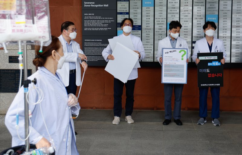 안석균 연세대학교 의과대학 비상대책위원장(왼쪽 첫번째)을 비롯한 교수들이 외래 진료 휴진에 들어간 30일 서울 서대문구 세브란스병원 본관 앞에서 의대정원 확대 등 정부 의료개혁 원점 재논의를 촉구하며 피켓 시위를 준비하는 가운데 한 환자가 이를 지켜보고 있다. 2024.4.30/뉴스1 ⓒ News1 안은나 기자