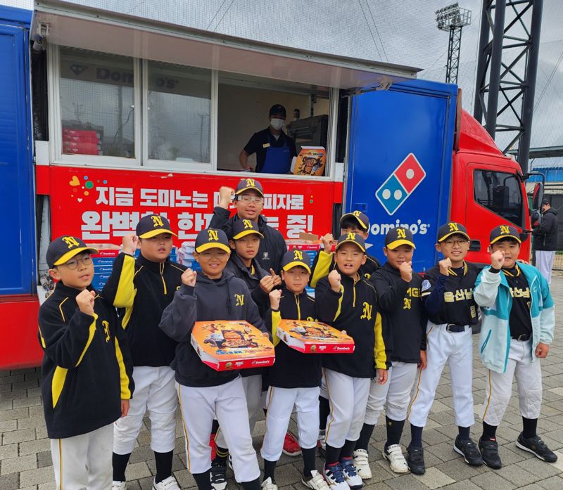도미노피자기 전국 리틀야구대회에 출동한 파티카 앞에서 어린이 야구 선수들이 포즈를 취하고 있다.