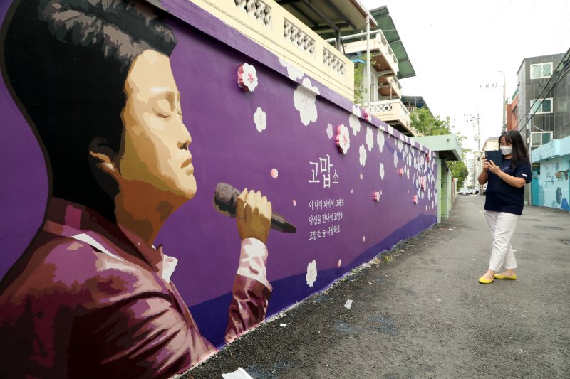 경북 김천예고 옆 교동연화지로 가는 골목길에 조성된 '트바로티 김호중 소리길'에서 팬카페 '아리스' 한 회원이 담장 벽화에 그려진 김호중의 그림을 카메라에 담고 있다. 뉴스1