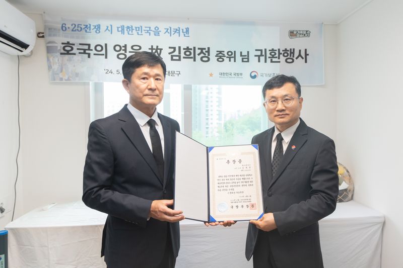 이근원 국방부 유해발굴감식단장이(사진 오른쪽) 30일 서울시 서대문구에 있는 유가족 자택에서 고 김희정 중위의 '호국의 영웅 귀환 행사'를 갖고 유가족 대표(왼쪽)에게 고인의 은성무공화랑훈장증을 전달하고 있다. 사진=국유단 제공