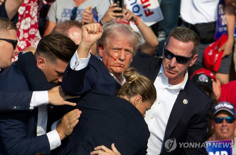 지난 13일(현지시간) 미국 펜실베이니아주 버틀러에서 유세 도중 날아온 총탄에 귀를 맞아 부상을 입은 도널드 트럼프 전 미 대통령이 비밀경호국 요원들에 둘러싸여 피신하는 사이에 지지자들에게 주먹을 쥐어 보이고 있다.AFP연합뉴스