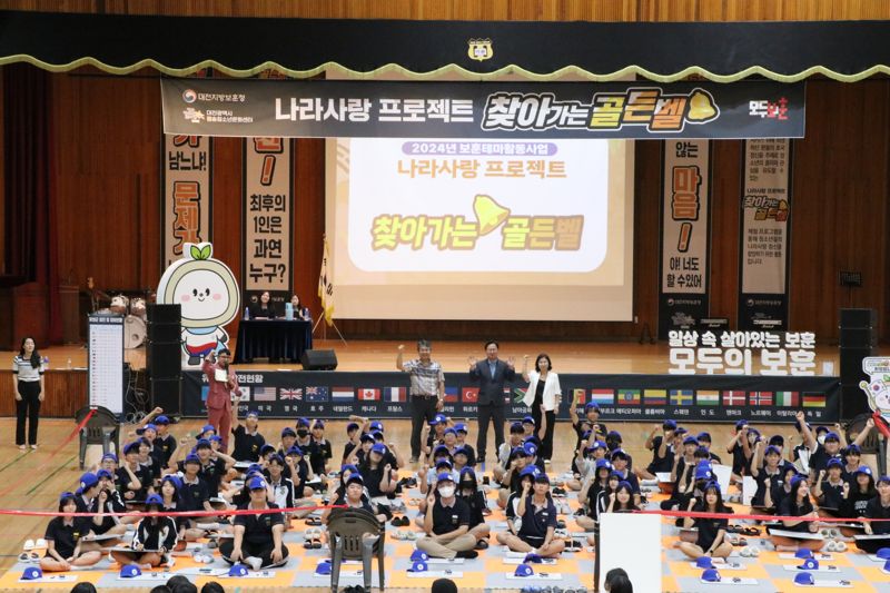 16일 오후 대전신탄진중학교에서 진행된 ‘나라사랑 프로젝트 찾아가는 골든벨’에서 100인의 학생들이 문제를 기다리고 있다. 뒷줄 좌측부터 이재홍 대전신탄진중학교 교장, 강만희 대전지방보훈청장, 김지연 평송문화센터장. 사진=국가보훈부 제공