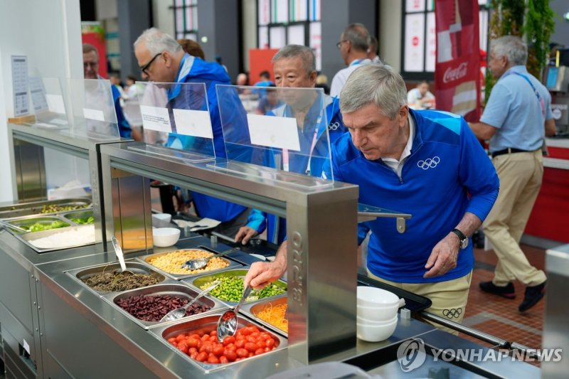 German International Olympic Committee (IOC) President Thomas Bach tries food from a salad bar while touring at the Olympic Village, in Paris on July 22, 2024, ahead of the 2024 Paris 2024 Olympic Games (Photo by David Goldman / POOL / AFP)