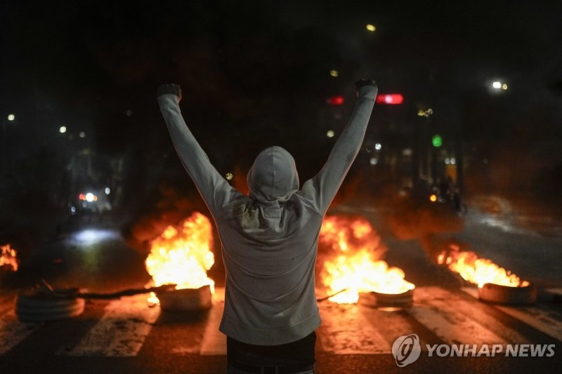 차베스상 깨부순 성난민심…대혼돈 베네수엘라에 이젠 총성까지(종합) A protestor raises his arms in front of tires on fire in Caracas, Venezuela, Monday, July 29, 2024, the day after the presidential election. (AP Photo/Matias Delacroix)