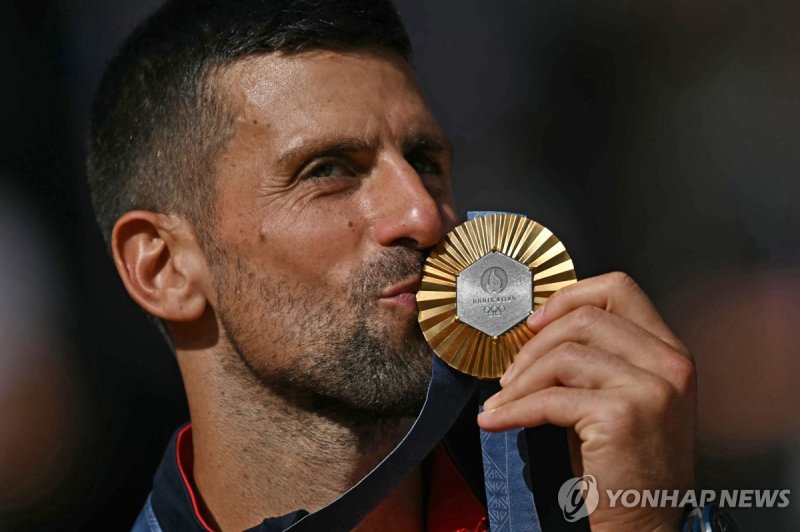 TOPSHOT - Gold medallist, Serbia's Novak Djokovic kisses his medal on the podium at the presentation ceremony for the men's singles tennis event on Court Philippe-Chatrier at the Roland-Garros Stadium during the Paris 2024 Olympic Games, in Paris on August 4, 2024. (Photo by CARL DE SOUZA / AFP) /사진