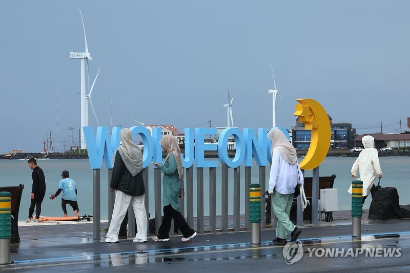 제주시 구좌읍 월정해수욕장에서 외국인 관광객들이 비가 내리는 해변을 거닐고 있다. 단기 방문 관광객과 구분되는 제주지역 3개월 이상 거주 외국인은 2025년 3만447명으로 전년보다 64명 감소했다. 사진=연합뉴스