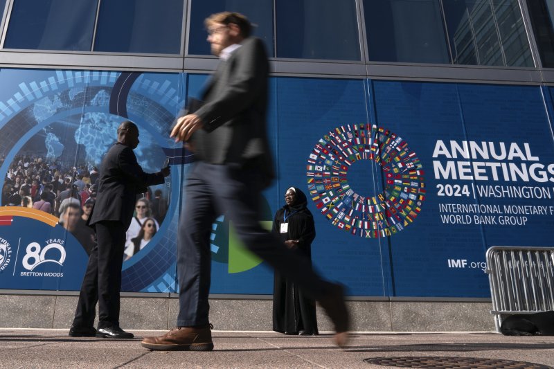 Delegates walk by an IMF banner, during the World Bank/IMF Annual Meetings at the International Monetary Fund (IMF) headquarters in Washington, Monday, Oct. 21, 2024. (AP Photo/Jose Luis Magana)