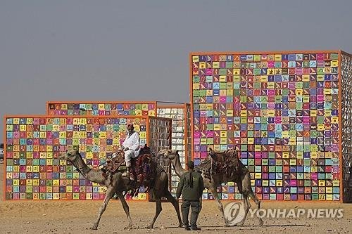 이집트 피라미드 앞에 우뚝 선 '한글 신전'…강익중 작품 공개 이집트 카이로 기자 피라미드 유적지에서 열린 '포에버 이즈 나우' 전시에서 낙타를 탄 관광 가이드가 강익중의 '네 개의 신전' 앞을 지나는 모습[AP=연합뉴스]