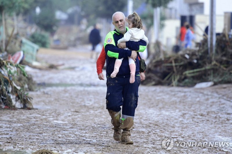대홍수 뒤 "기후변화 대응 안일했다" 비판 목소리 TOPSHOT - A Civil Protection member carries a child in a street covered in mud in a flooded area in Picanya, near Valencia, eastern Spain, on October 30, 2024. Floods triggered by torrential rains in Spain's eastern Valencia region has left 51 people dead, rescue services
