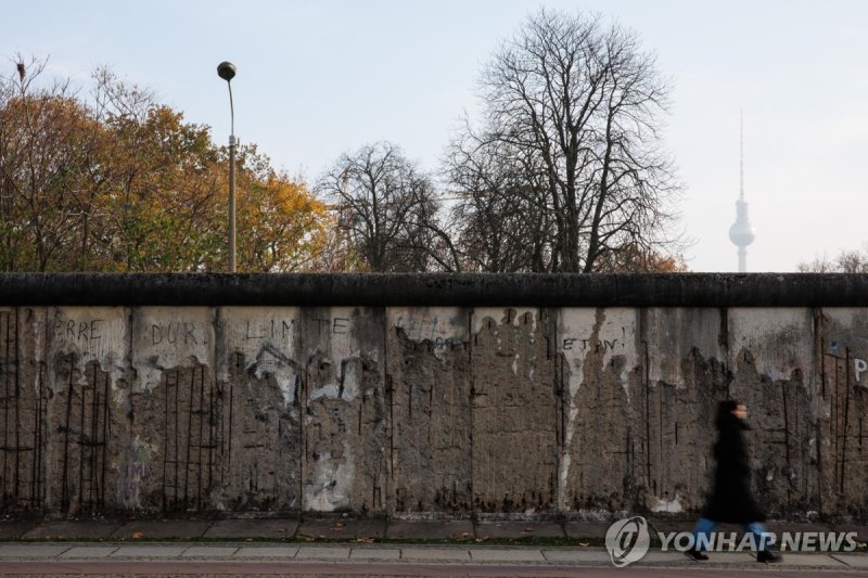오늘날까지 남아 있는 베를린 장벽 구간 앞을 걷는 현지 주민 epa11711703 A passer-by walks along remains of the Berlin Wall after a commemorative event on the 35th anniversary of the fall of the Berlin Wall in Berlin, Germany, 09 November 2024. The Berlin Wall surrounded West Berlin for 155 kilometers and divided the city fro