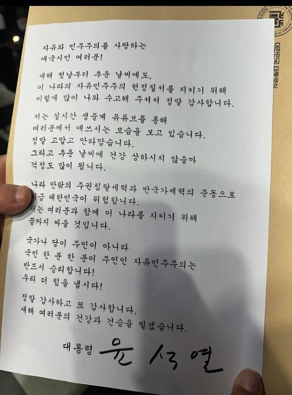[서울=뉴시스] 윤석열 대통령이 1일 오후 7시30분께 서울 용산구 한남동 대통령 관저 앞 도로에서 철야집회를 하는 지지자들에게 직접 서명한 새해인사 및 감사인사글을 전했다. 2025.01.01. *재판매 및 DB 금지