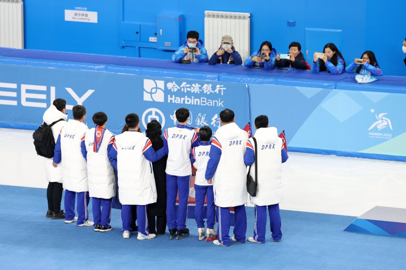 하얼빈 동계아시안게임 피겨 페어에서 은메달을 차지한 북한 렴대옥·한금철이 12일 중국 헤이룽장성 하얼빈 빙상훈련센터 다목적홀에서 열린 시상식을 마치고 코치진과 함께 인공기를 펼치고 사진을 찍고 있다. 2025.2.12/뉴스1 ⓒ News1 이승배 기자