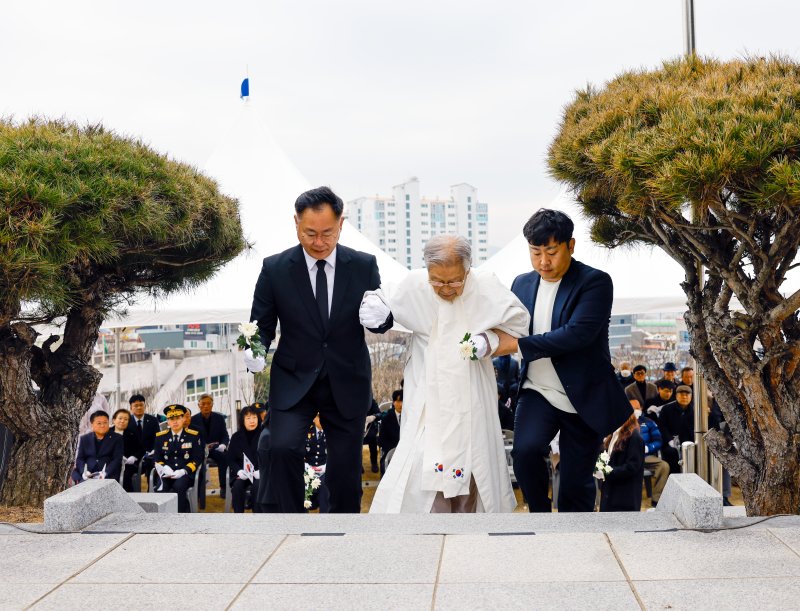 [칠곡=뉴시스] 장진홍 의사의 손자 장상규(86) 씨가 김재욱(왼쪽) 칠곡군수의 부축을 받으며 헌화대로 오르고 있다. (사진=칠곡군 제공) 2025.03.03 photo@newsis.com *재판매 및 DB 금지