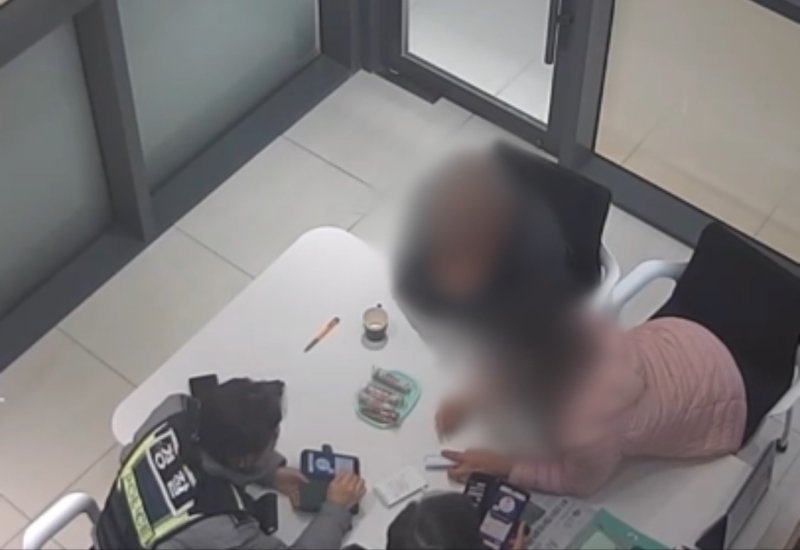 지난 13일 부산 북구 한 은행에서 보이스피싱이 의심된다는 신고를 받고 출동한 경찰과 은행 고객 60대 여성이 휴대전화를 살펴보고 있다.(부산경찰청 제공 CCTV 갈무리. 재판매 및 DB 금지)