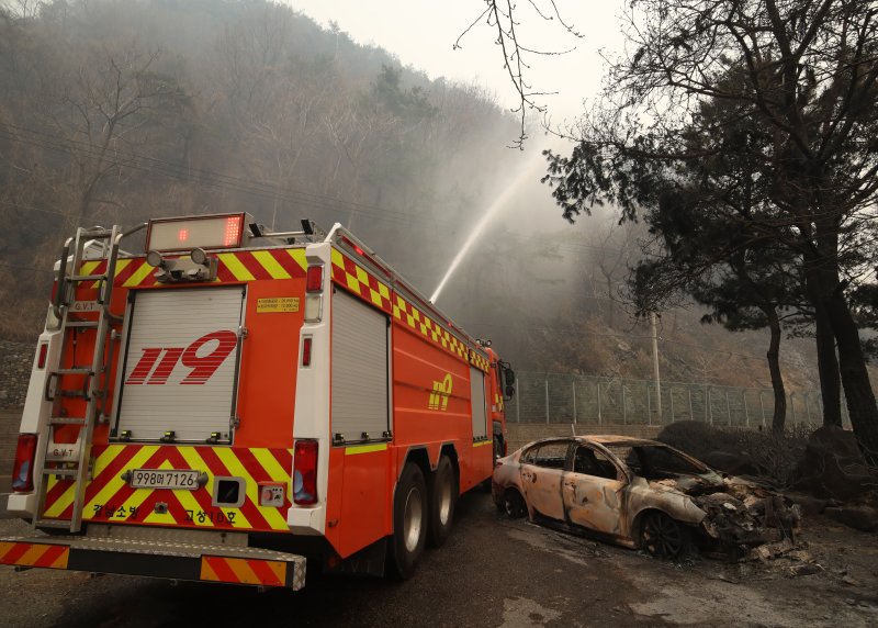 경남 산청 대형 산불이 사흘째로 접어든 23일 오전 산청군 시천면 일대에서 소방이 산불로 인해 전소된 승용차 뒤로 잔불을 정리하고 있다. 2025.3.23/뉴스1 ⓒ News1 윤일지 기자