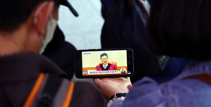 [서울=뉴시스] 박주성 기자 = 4일 오전 서울 용산구 서울역 역사에서 시민들이 핸드폰으로 윤석열 전 대통령 탄핵심판 선고를 시쳥하고 있다. 2025.04.04. park7691@newsis.com