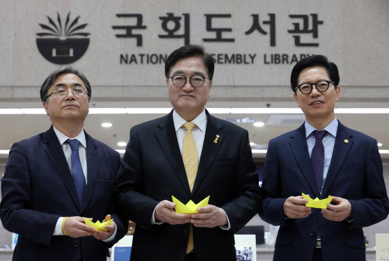 [서울=뉴시스] 고승민 기자 = 우원식(가운데) 국회 의장이 16일 서울 여의도 국회도서관에서 열린 '기억의 물결, 책으로 흐르다' 세월호 11주기 특별도서전에서 노란 종이배를 들고 기념촬영하고 있다. 2025.04.16. kkssmm99@newsis.com