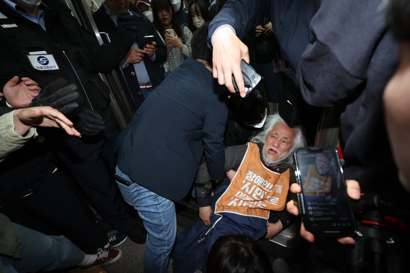 박경석 전국장애인차별철폐연대(전장연) 대표가 21일 서울 지하철 4호선 혜화역 동대문 방면 승강장에서 제62차 '출근길 지하철 탑니다' 시위를 벌이던 중 이를 저지하던 경찰·서울교통공사 직원 등과 충돌하며 열차 입구에 넘어져 있다. 전장연의 출근길 지하철 탑승 시위는 지난해 4월8일 이후 1년여 만이다. 2025.4.21/뉴스1 ⓒ News1 이동해 기자