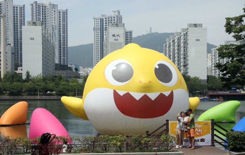 [부산=뉴시스] 하경민 기자 = 부산 해운대구 APEC나루공원을 찾은 한 가족이 2일 오전 수영강 위에 설치된 높이 13m, 폭 17.5m의 초대형 아기상어 부유형 조형물을 배경으로 기념사진을 찍고 있다. 이 조형물은 한 달간 전시된다. 2023.07.02. yulnetphoto@newsis.com