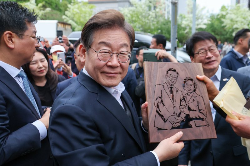 이재명 더불어민주당 대통령 후보가 2차 골목골목 경청투어에 나선 5일 오후 충북 진천군의 혁신도시 상가를 찾아 한 시민으로부터 이 후보와 김혜경 여사를 나무판에 각인한 그림판을 선물받고 있다. 2025.5.5/뉴스1 ⓒ News1 안은나 기자