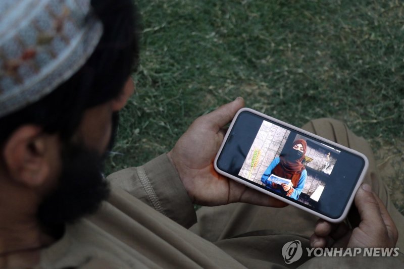 얼굴을 가린 여성 앵커의 뉴스 진행 장면을 보는 아프간 남성 (출처=연합뉴스)