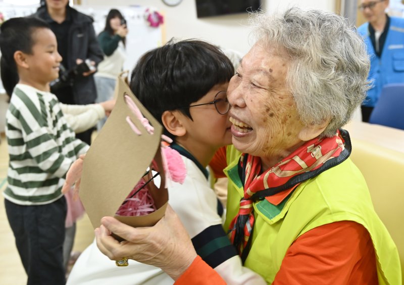 [수원=뉴시스] 김종택 기자 = 어버이날을 하루 앞둔 7일 경기 수원시 팔달노인복지관을 찾은 어린이들이 고사리 손으로 어르신들에게 카네이션을 달아드린 뒤 포옹하고 있다. 2025.05.07. jtk@newsis.com