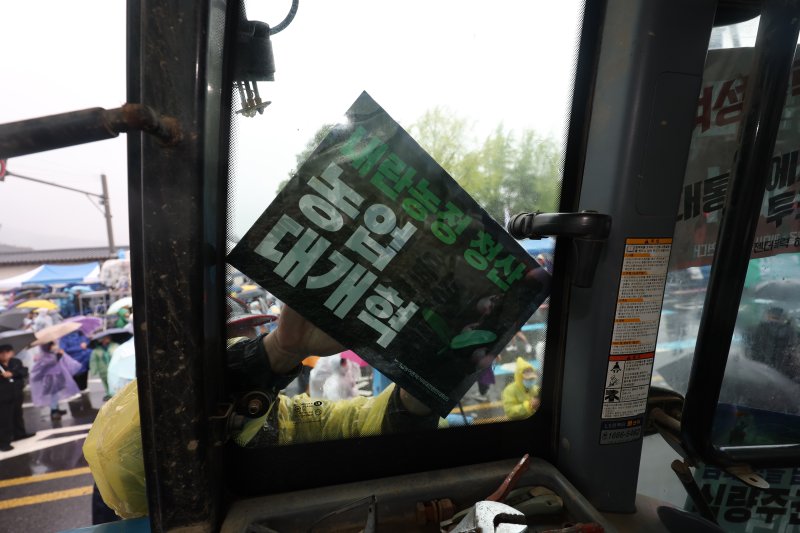 [서울=뉴시스] 김명년 기자 = 10일 오후 서울 종로구 경복궁 동십자각 인근에서 열린 내란청산·사회대개혁 비상행동 주최 사법부 정치개입 규탄 집회에서 한 농민이 도착한 전국농민회총연맹 트랙터에 피켓을 붙이고 있다. 2025.05.10. kmn@newsis.com