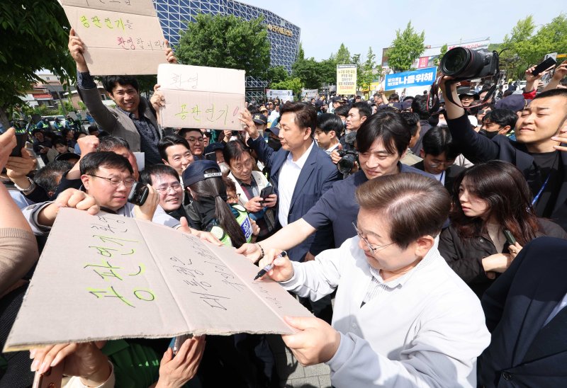 [전주=뉴시스] 조성봉 기자 = 민심을 청취하는 '경청 투어'에 나선 이재명 더불어민주당 대선후보가 7일 전북 전주시 완산구 풍남문 인근에서 공판연기를 환영하는 지지자의 응원 피켓에 사인을 해주고 있다. '공판연기 환영, 대통령은 국민이 뽑습니다'라고 적힌 피켓에 이 후보는 '맞습니다' 라고 쓰고 있다. 2025.05.07. suncho21@newsis.com