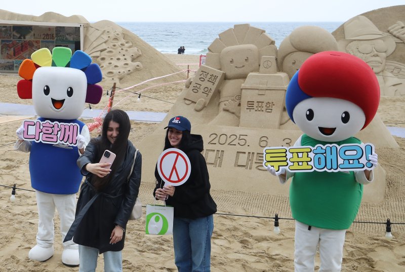 제21대 대통령선거를 앞둔 15일 오후 부산 해운대해수욕장에서 정책·공약에 대한 관심과 투표 참여를 높이기 위해 부산시선관위의 '모래로 만나는 대통령선거' 홍보 캠페인이 진행되는 가운데 외국인 관광객들이 모래작품 앞에서 셀카를 찍고 있다. 2025.5.15/뉴스1 ⓒ News1 윤일지 기자
