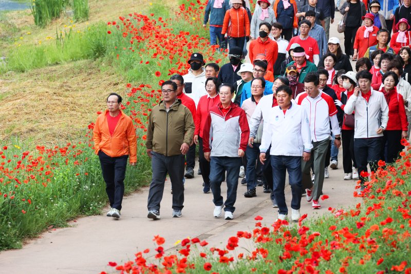 [괴산=뉴시스] 24일 '2025 빨간맛페스티벌'의 대표 프로그램 '빨간꽃길 괴산 걷기대회'가 열린 충북 괴산군 동진천변에서 참가자들이 붉게 물든 양귀비 꽃길을 따라 봄 정취를 만끽하고 있다. (사진=괴산군 제공) 2025.05.24. photo@newsis.com *재판매 및 DB 금지