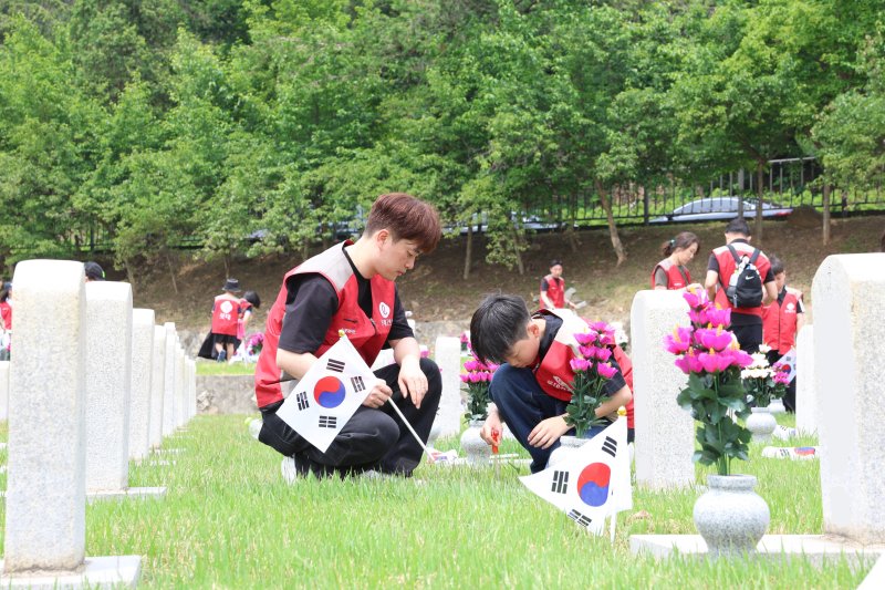 [서울=뉴시스] 롯데건설 '샤롯데 봉사단'이 묘비 옆에 태극기를 꽂고 있다. (사진=롯데건설 제공)