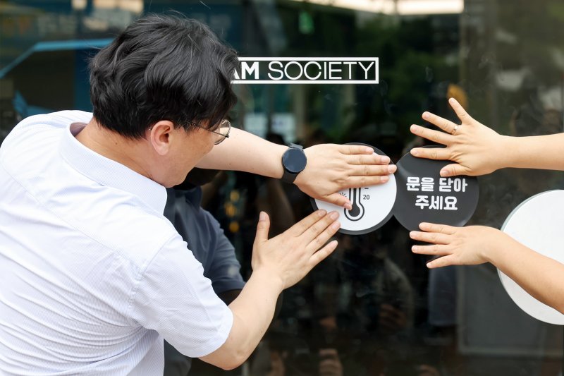 이원주 산업통상자원부 대변인이 2일 오후 서울 중구 명동 온드림 소사이어티에서 열린 '여름철 에너지절약 캠페인'에 참석해 출입문에 개문냉방 자제 스티커를 붙이고 있다. 2025.7.2/뉴스1 ⓒ News1 민경석 기자