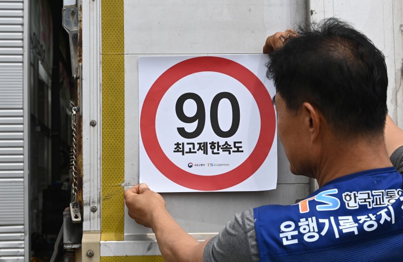 [화성=뉴시스] 김종택 기자 = 23일 경기 화성시 한 화물차 운행기록장치(DTG)점검센터에서 관계자가 화물차 후면에 최고 제한속도 스티커를 부착하고 있다. 국토교통부와 한국교통안전공단(TS)은 오늘부터 총중량 3.5t(톤)을 초과하는 화물차를 대상으로 ‘최고 제한속도(90㎞/h) 스티커’를 부착하는 시범사업을 실시했다. 2025.07.23. jtk@newsis.com